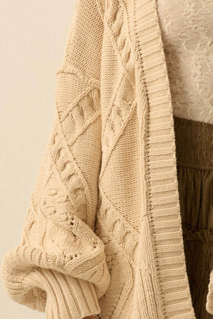 Close-up of a beige knitted sweater with cable pattern on a neutral background