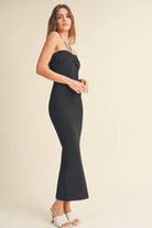 Model wearing a black halter dress with a twisted front detail, standing confidently with wavy hair.
