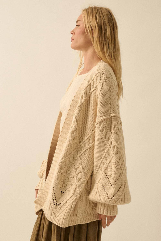 Woman wearing a beige cable knit cardigan against a plain background