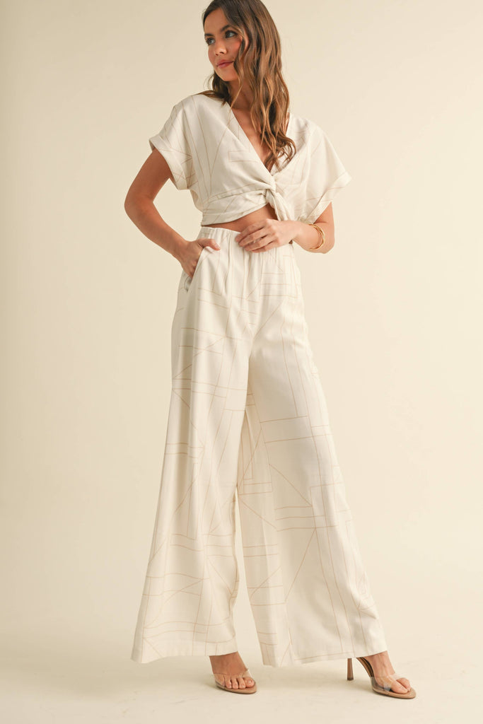 Woman wearing a cream two-piece set with geometric line print, knotted crop top, and wide-leg pants.