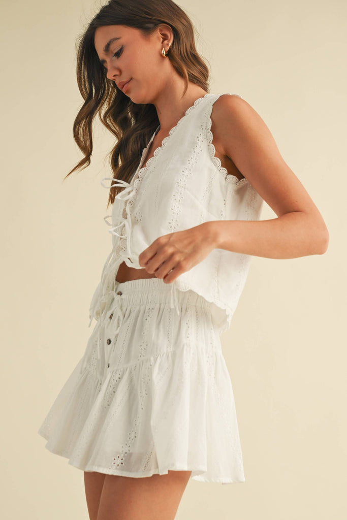 White embroidered cotton set with sleeveless tie-front top and tiered mini skirt featuring scalloped lace trim
