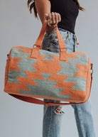 Wool woven orange and sage green weekender bag with geometric pattern, held by woman in jeans and black top