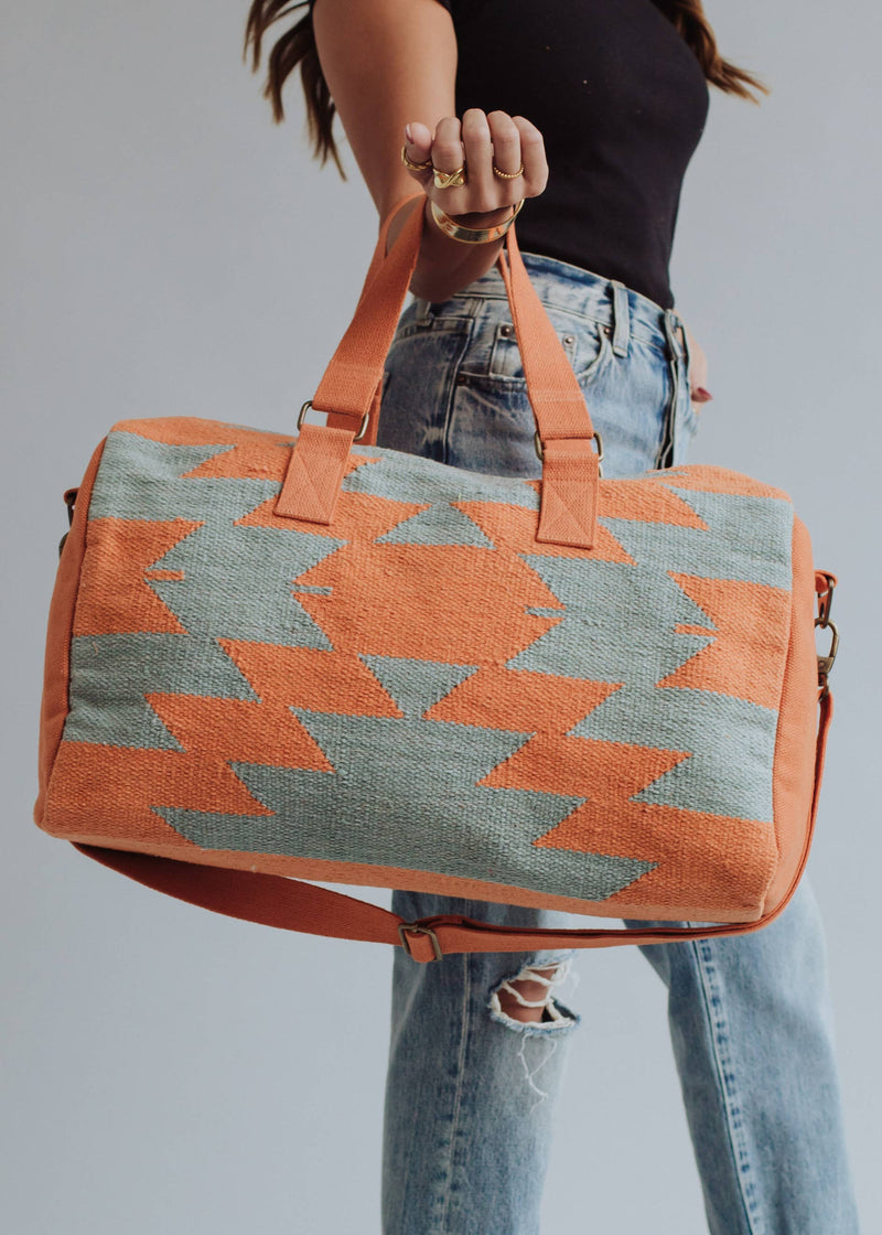 Wool woven orange and sage green weekender bag with geometric pattern, held by woman in jeans and black top
