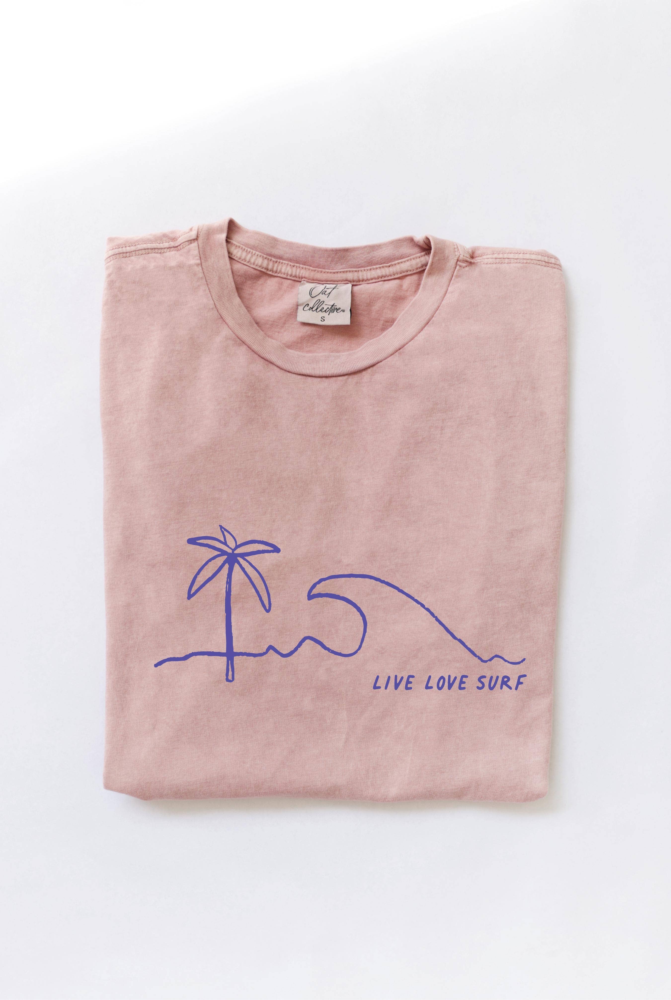 Folded soft pink-colored t-shirt with a blue minimalist palm tree, wave, and "LIVE LOVE SURF" graphic.