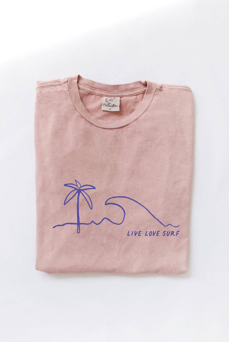 Folded soft pink-colored t-shirt with a blue minimalist palm tree, wave, and "LIVE LOVE SURF" graphic.