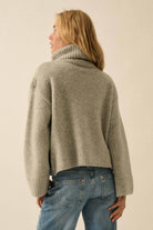 Person wearing a gray sweater and blue jeans against a plain background