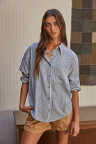 Woman wearing a long-sleeve striped button-up shirt with front pocket, styled casually with rolled cuffs and jeans.