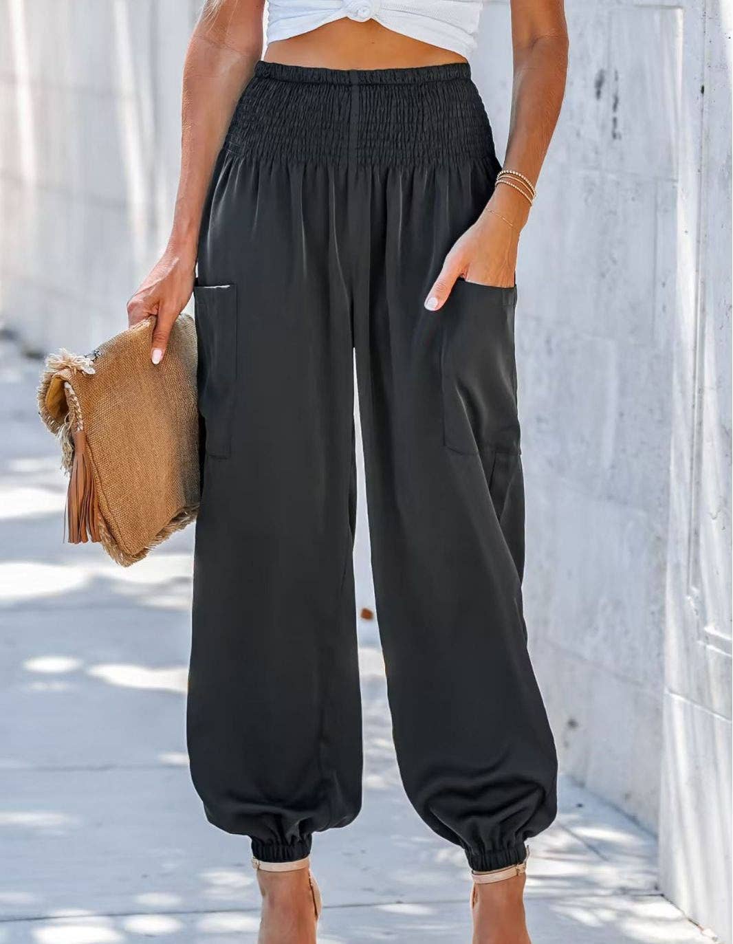 Woman wearing Serenity High-Waist Comfort Pants in beige and olive colors, paired with a white crop top and heels, carrying a decorative clutch.