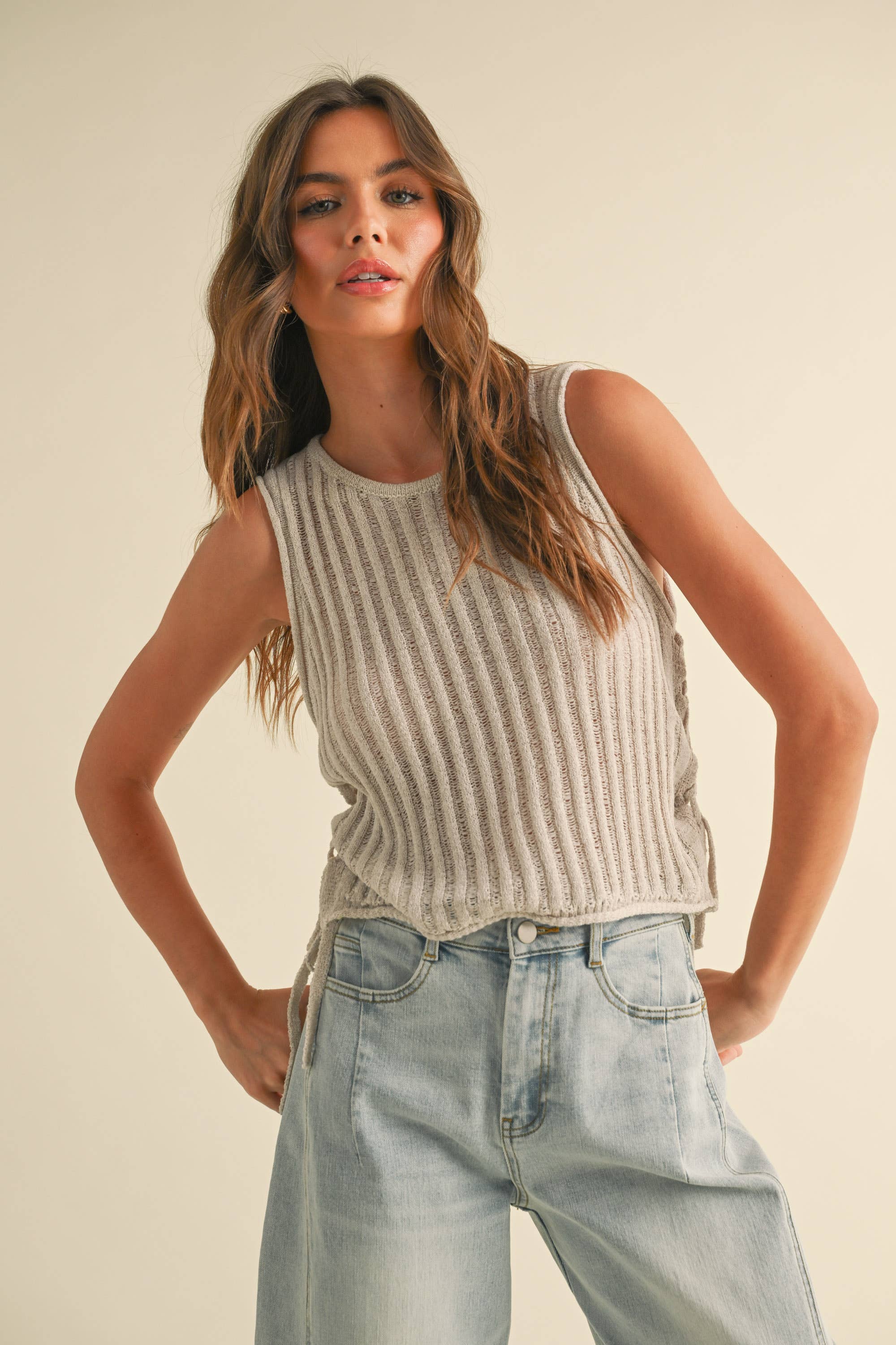 Woman wearing a striped sleeveless top and light blue jeans against a plain background