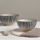 Two ceramic bowls with black stripes on a neutral background