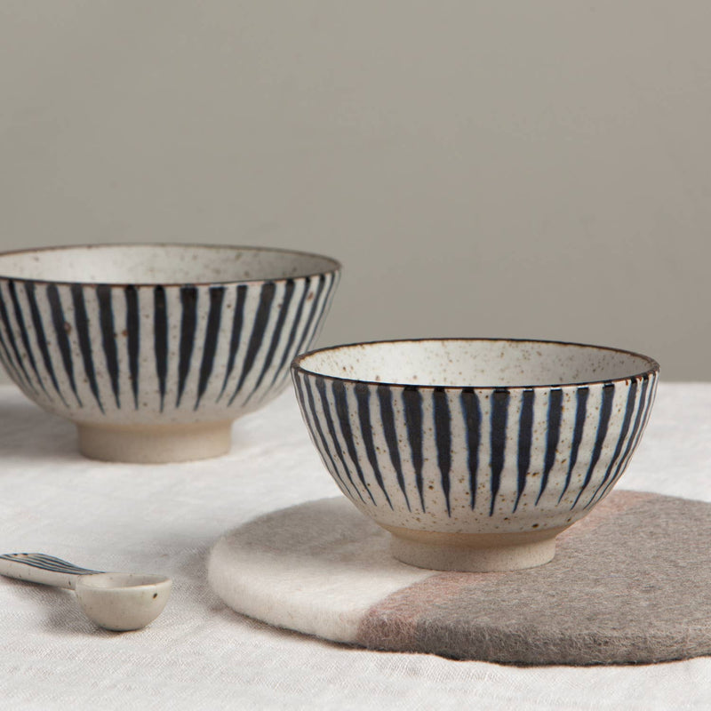 Two ceramic bowls with black stripes on a neutral background