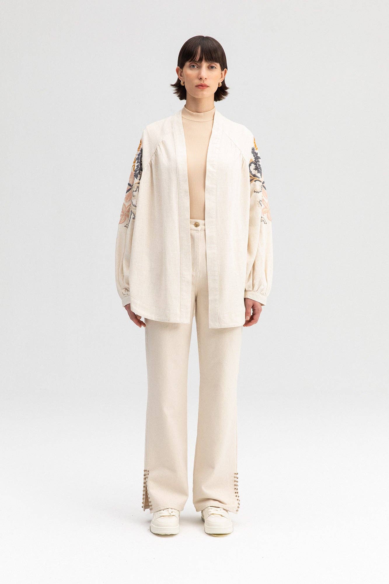 Back view of a cream-colored kimono jacket with colorful floral embroidery, worn with matching light trousers.