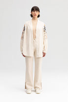 Back view of a cream-colored kimono jacket with colorful floral embroidery, worn with matching light trousers.