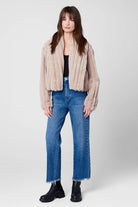 Woman wearing a beige jacket, black top, blue jeans, and black shoes on a white background