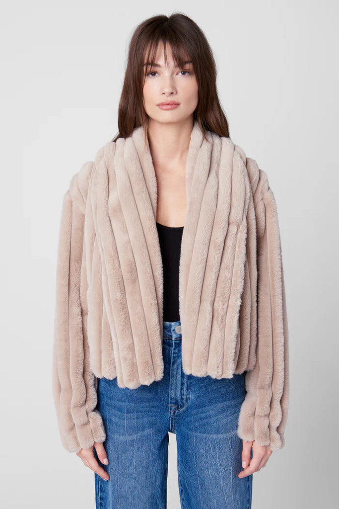 Woman wearing a beige fur coat over a black top and blue jeans on a white background