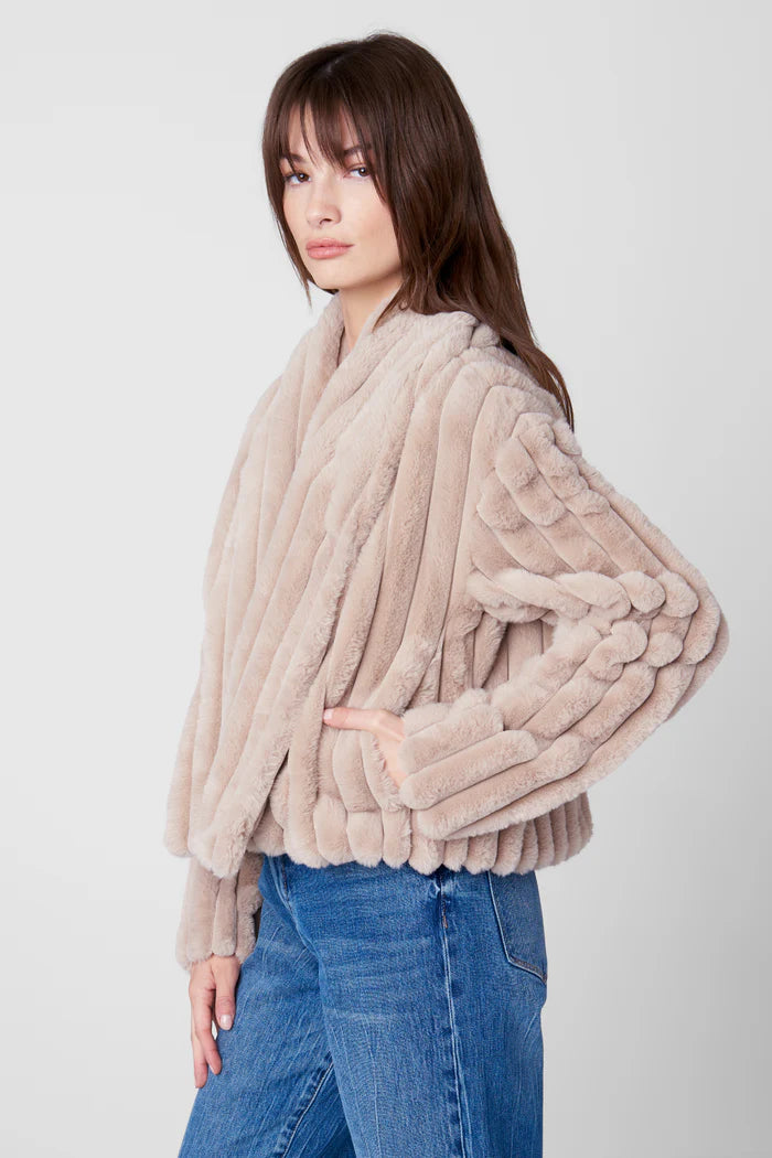 Woman wearing a beige fur coat and blue jeans on a white background