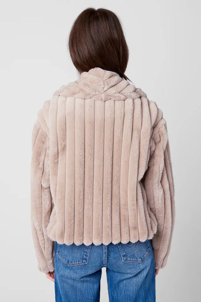 Person wearing a beige faux fur jacket and blue jeans on a white background