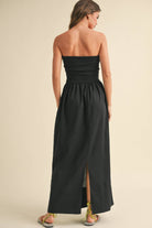 Woman wearing a black strapless maxi dress with a fitted bandeau bodice and flowy skirt.