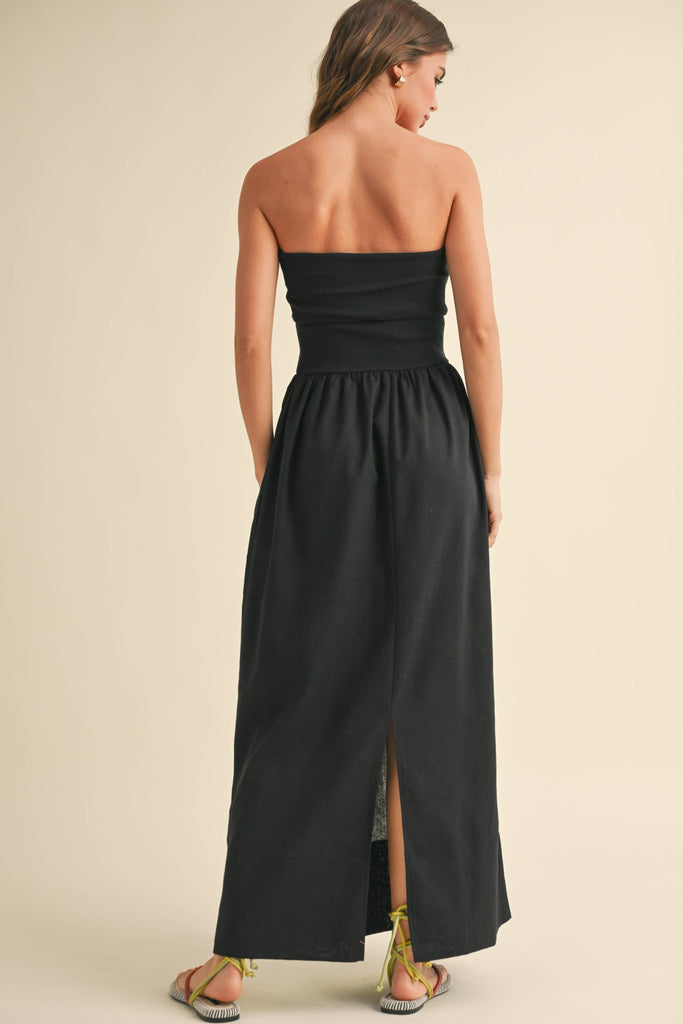 Woman wearing a black strapless maxi dress with a fitted bandeau bodice and flowy skirt.