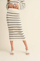 Woman wearing a high-waisted, ivory and black striped knit midi skirt with slide sandals.