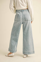 Woman wearing wide-leg light denim pants with a tie-front waist, paired with a white blouse and ballet flats.