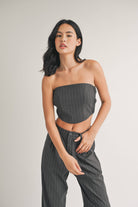 Woman wearing a strapless navy pinstriped crop top with tailored pleated pants.