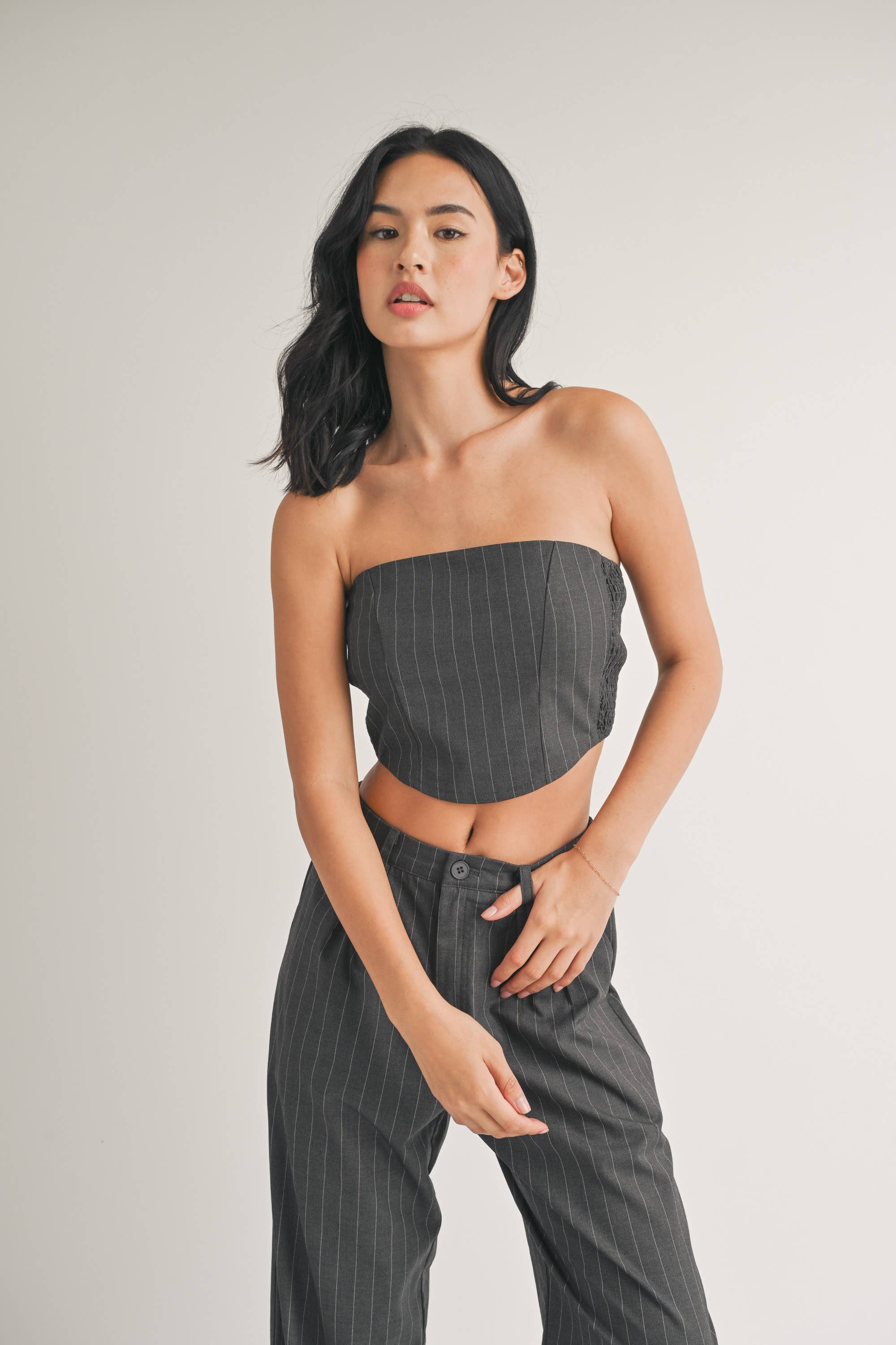 Woman wearing a strapless navy pinstriped crop top with tailored pleated pants.