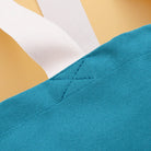 Teal tote bag with “Sunshine Appreciation Society” in white text, held by a person in a green dress at the beach