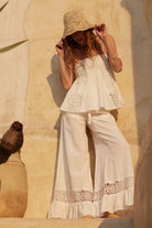Woman wearing white embroidered cami top with eyelet detail and flared hem in natural sunlight.