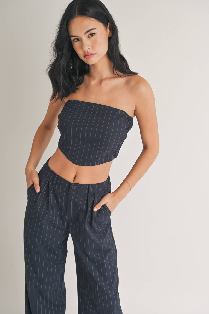 Woman wearing a strapless navy pinstriped crop top with tailored pleated pants.