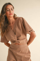 Woman wearing a two-piece striped set with a twist-front crop top and wide-leg pants in cream and tan color options.