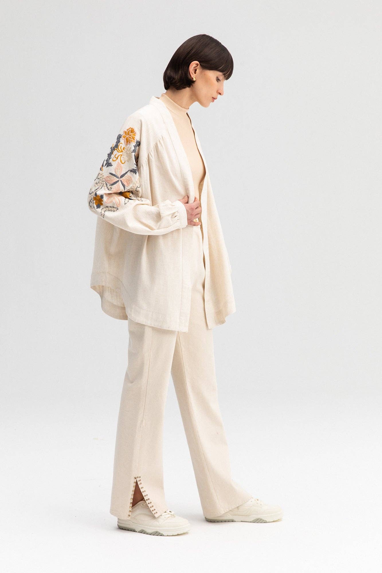 Back view of a cream-colored kimono jacket with colorful floral embroidery, worn with matching light trousers.