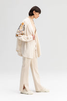 Back view of a cream-colored kimono jacket with colorful floral embroidery, worn with matching light trousers.