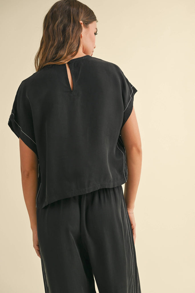 Model wearing a black two-piece lounge set with white contrast stitching, featuring a cap-sleeve top and drawstring wide-leg pants.