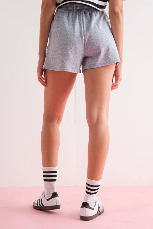 Close-up of a woman wearing gray elastic waist shorts with side zipper details.