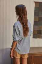 Woman wearing a long-sleeve striped button-up shirt with front pocket, styled casually with rolled cuffs and jeans.
