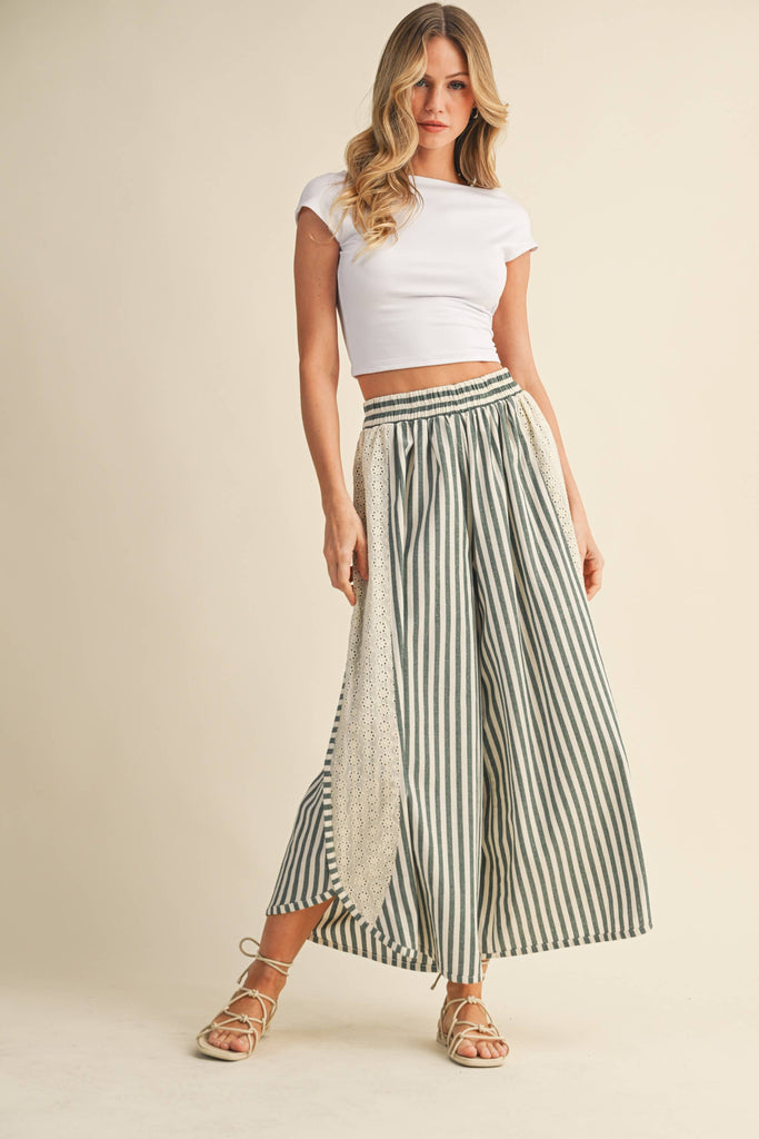 Woman wearing a white crop top and striped wide-leg pants on a beige background