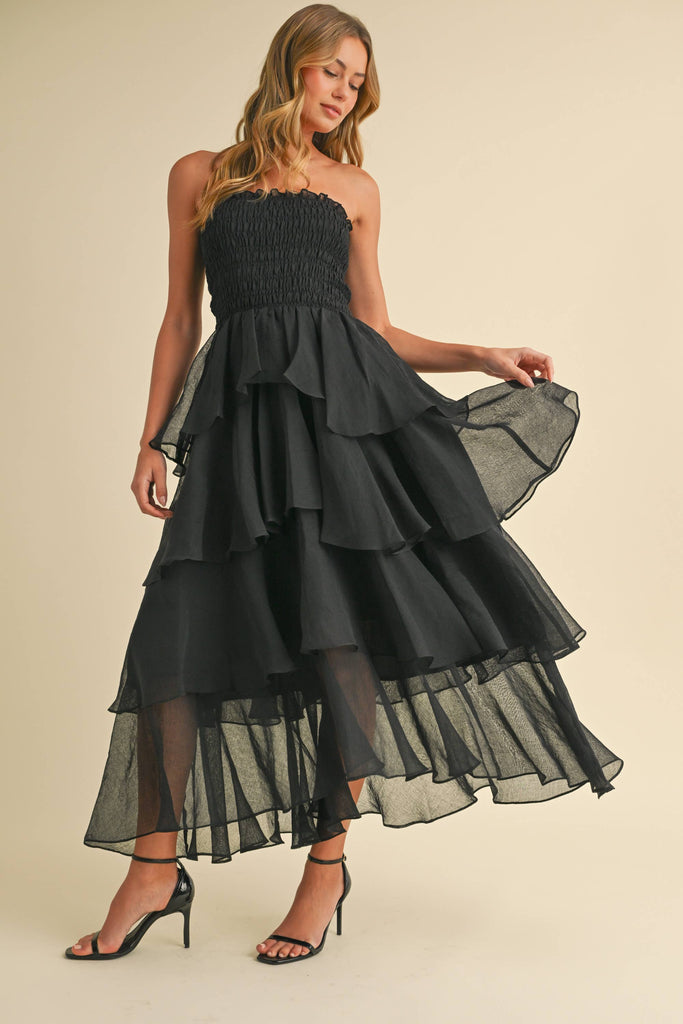 Woman wearing a strapless ruffled maxi dress with a smocked bodice, available in taupe and black.