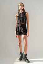 Woman wearing a black round neck sleeveless ladder knit crop top.