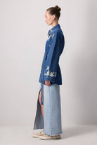 Model wearing a belted denim jacket with white floral embroidery and wide sleeves