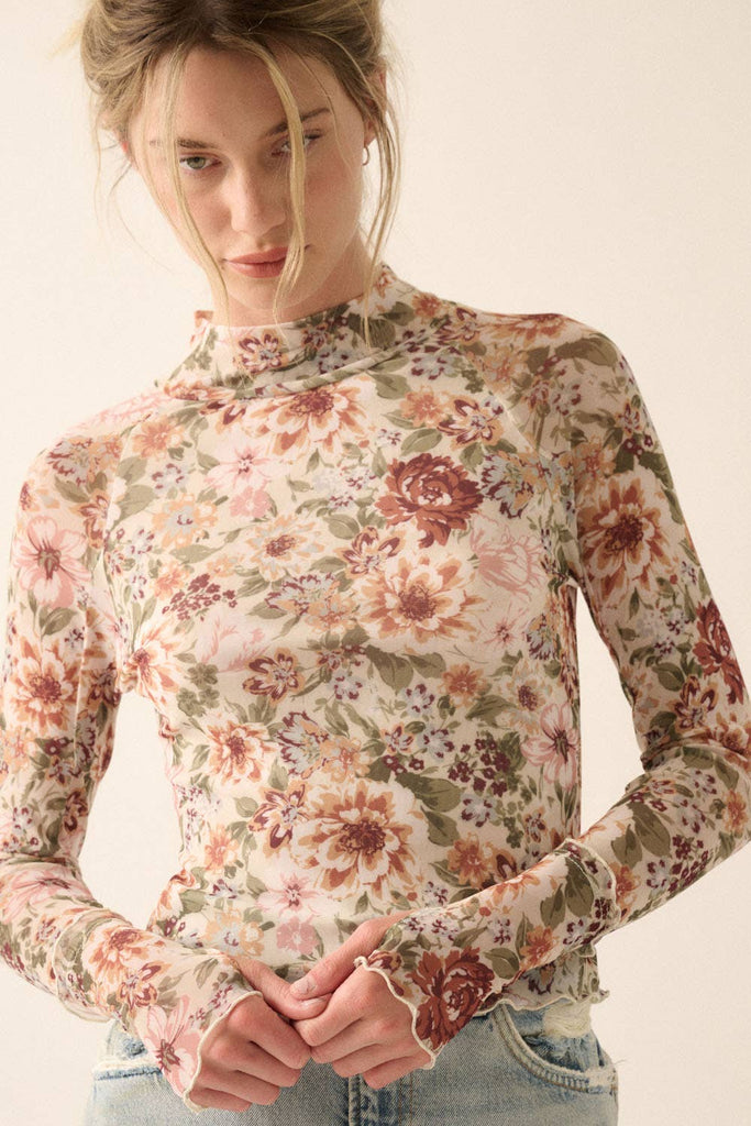 Woman wearing a sheer mesh floral long-sleeve top with mock neck and fitted silhouette.