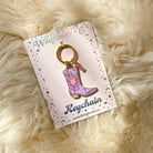 Flaming Cowgirl Boot Enamel Keychain on a decorative backing card.