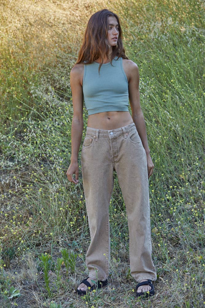 Woman wearing a fitted waffle-texture cropped tank top in green and white, styled with casual denim and neutral pants.