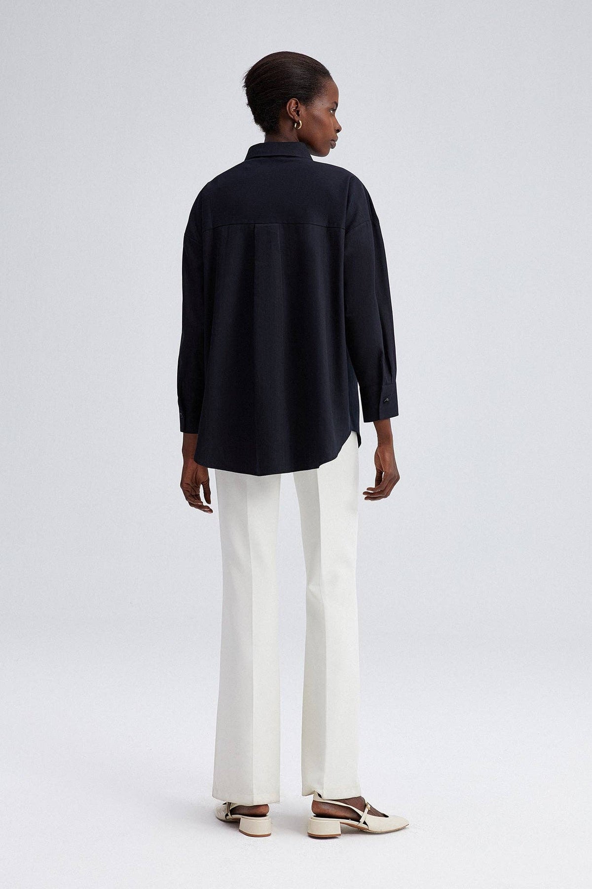 Model wearing black oversized shirt with cream embroidery on shoulders and front yoke.
