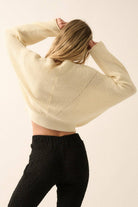 Woman wearing a cream lightweight knit sweater with wide sleeves and a cropped fit.