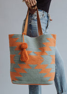 Tote bag with orange and sage green zigzag design and tassel, styled with denim jeans