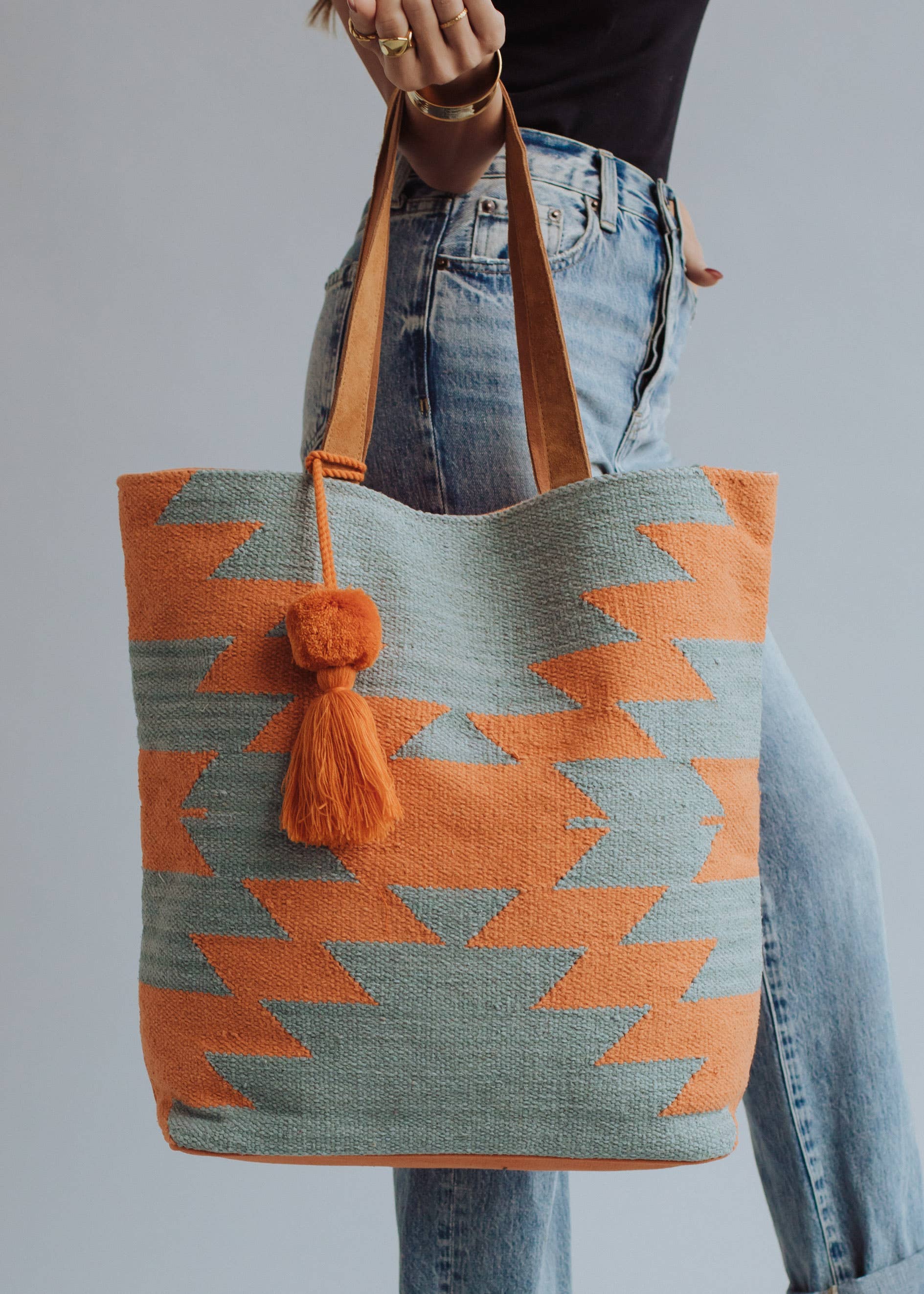 Tote bag with orange and sage green zigzag design and tassel, styled with denim jeans