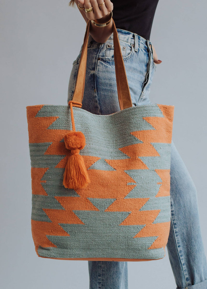 Tote bag with orange and sage green zigzag design and tassel, styled with denim jeans