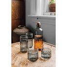 Set of glass tumblers on a wooden table with a bottle of amber liquid.