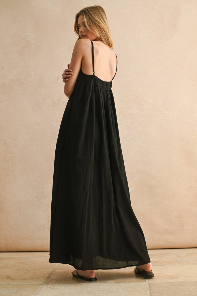 Model in black embroidered maxi dress with thin straps and flowy silhouette, featuring beige V-shaped stitching detail.